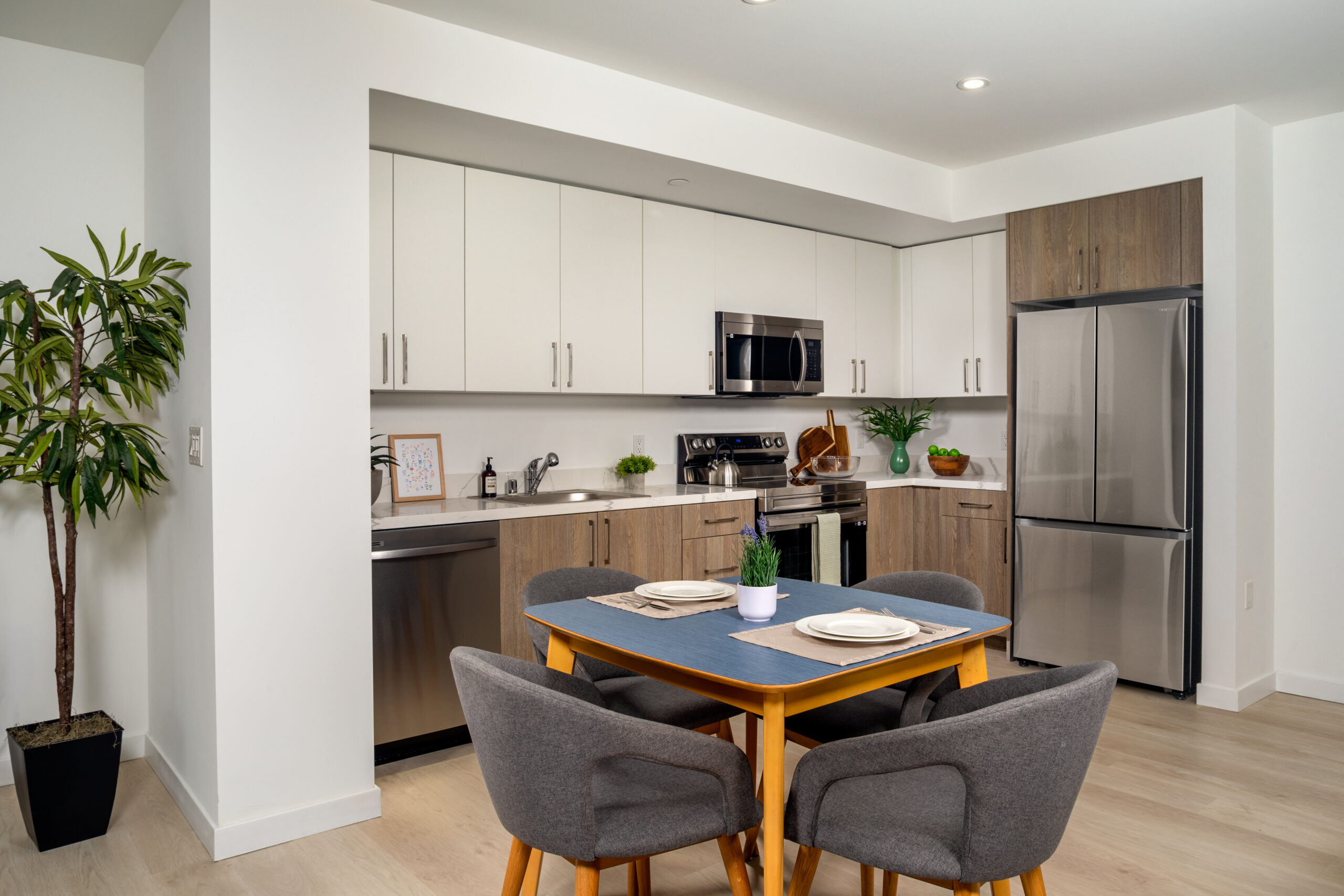 A dining area and kitchen with a table, white and brown cabinets, and stainless steel appliances.